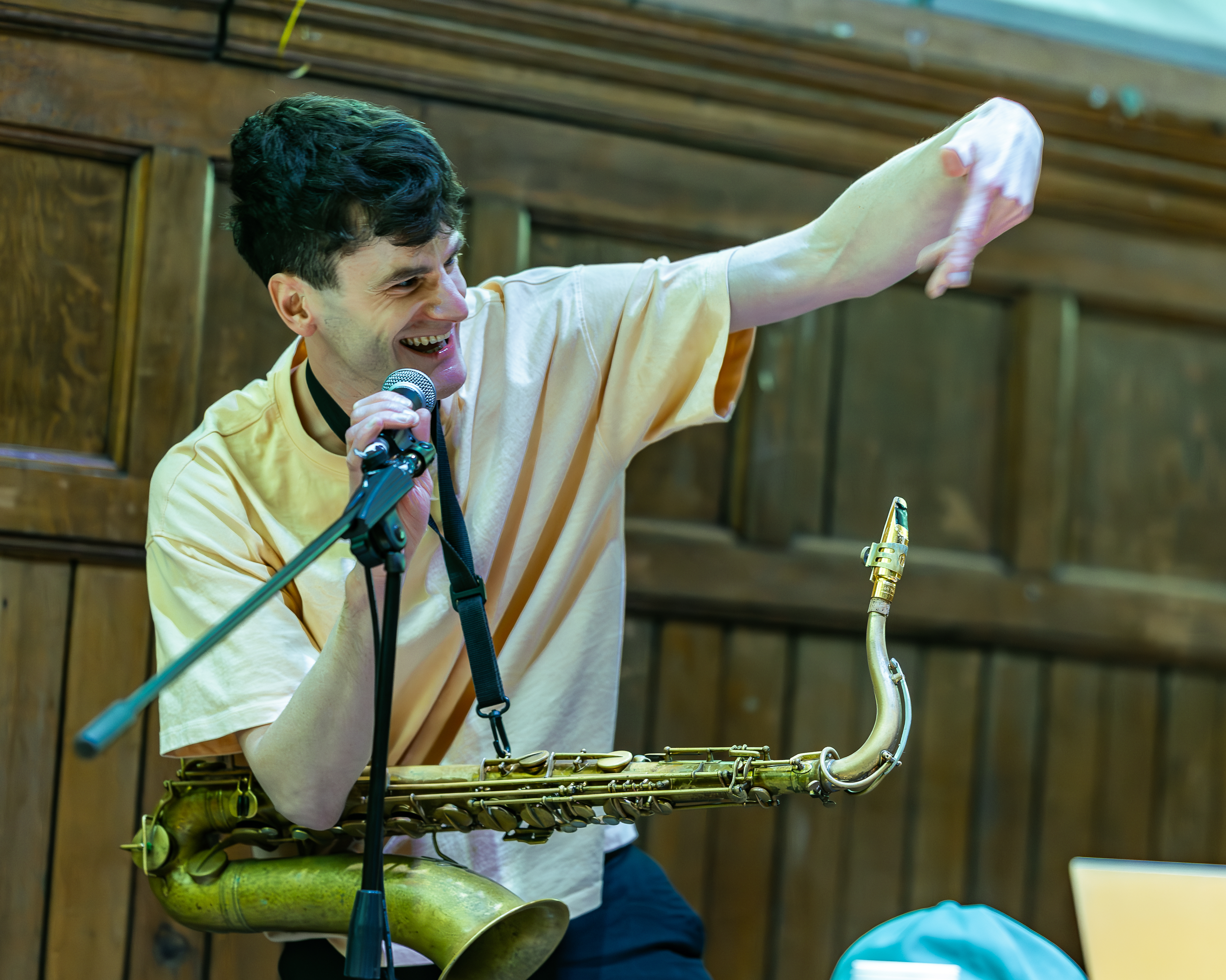 Tom Rigby performing — singing into a microphone while playing saxophone